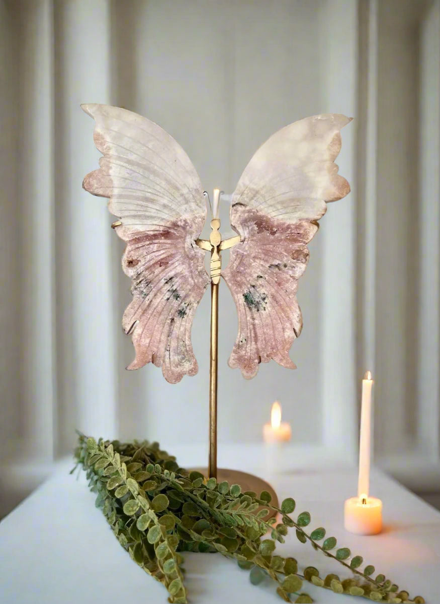 Decorative butterfly wings on a stand with candles and greenery in the background