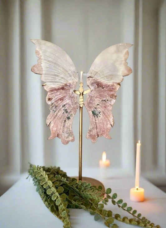 Decorative butterfly wings on a stand with candles and greenery in the background